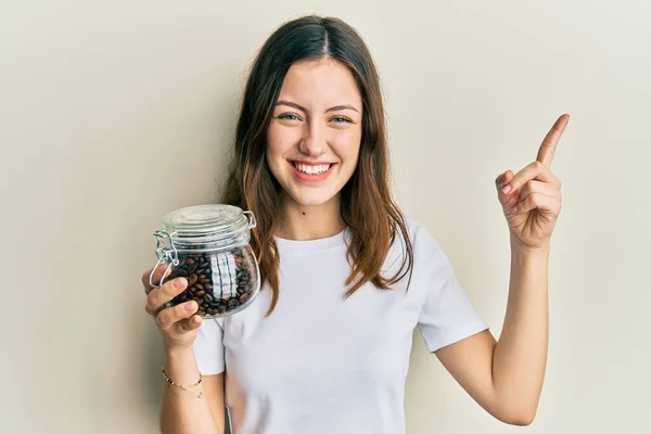 Kahve Çekirdeği Dolu Kavanozu Tutan Genç Esmer Kadın Gülümsüyor — Stok fotoğraf