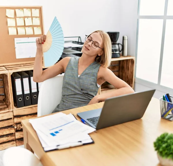 Ofiste çalışan genç sarışın kadın el fanı kullanıyor.