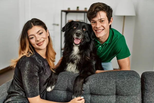 Genç, beyaz bir çift, mutlu bir şekilde gülümsüyor ve evde köpekleriyle koltukta oturuyor..