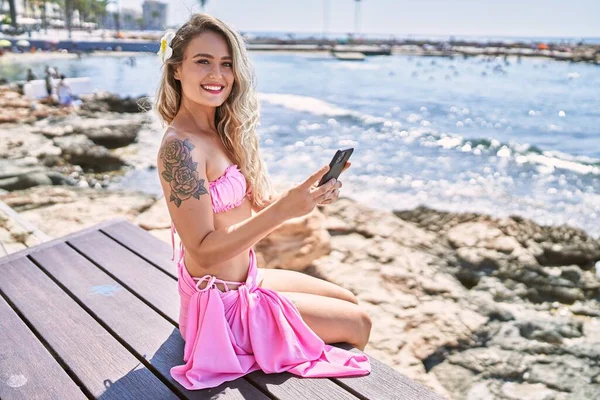 Młoda Blondynka Pomocą Smartfona Siedzi Ławce Plaży — Zdjęcie stockowe
