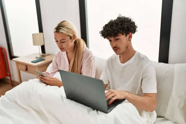 Unga Vackra Par Med Hjälp Laptop Och Smartphone Sitter Sängen — Stockfoto