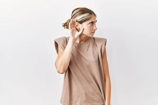若いブロンドの女性が孤立した背景の上に立ち 噂やゴシップに耳を傾けながら手で笑っている 聴覚障害の概念 — ストック写真