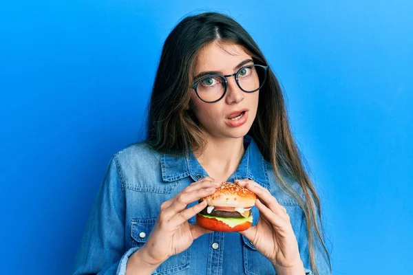 Young Caucasian Woman Eating Tasty Classic Burger Shock Face Looking — Stock Photo, Image