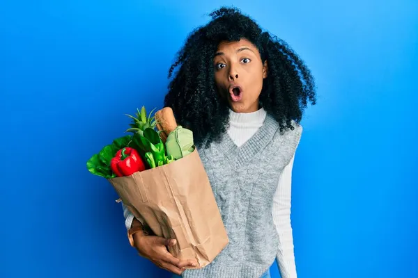 アフリカ系アメリカ人女性アフロヘア保持紙袋で食料品を怖がらせ 驚きのために口を開けて驚いて 不信の顔 — ストック写真