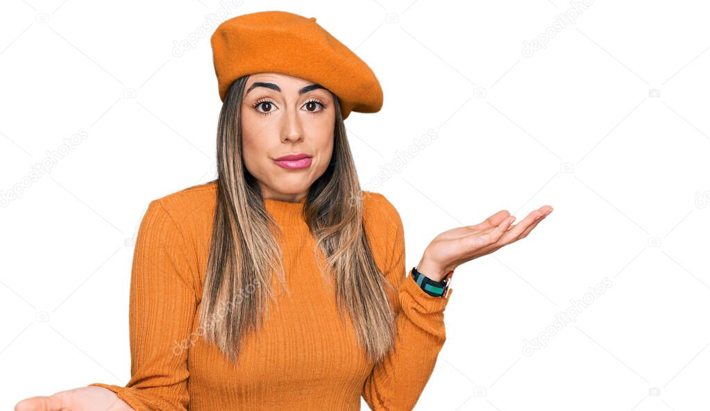 Young hispanic woman wearing french look with beret clueless and confused expression with arms and hands raised. doubt concept. 
