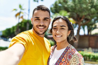 Genç Latin çift, mutlu bir şekilde gülümsüyor ve kucaklaşıyorlar. Kameranın önünde selfie çekiyorlar..