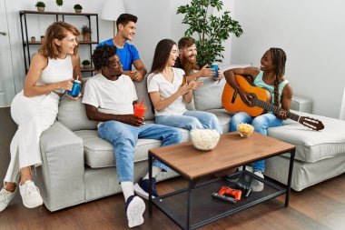 Mutlu gülümseyen ve evde klasik gitar çalan bir grup genç arkadaş..