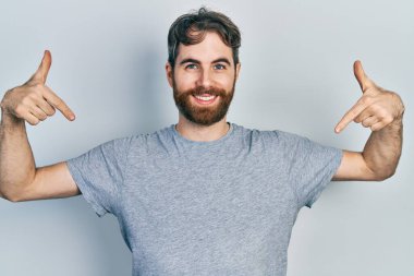 Sakallı, günlük gri tişörtlü, kendine güvenen, gülümseyen, kendini gururlu ve mutlu gösteren beyaz bir adam.. 