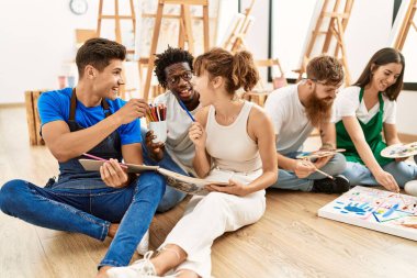 Bir grup insan resim stüdyosunda yerde otururken mutlu bir şekilde gülümsüyor..