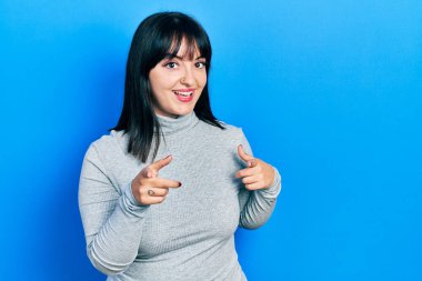 Gündelik kıyafetler giyen genç İspanyol kadın mutlu ve komik yüzüyle kamerayı işaret ediyor. iyi enerji ve titreşimler. 