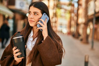 Genç İspanyol kadın akıllı telefondan konuşuyor ve şehirde kahve içiyor..