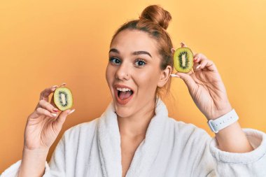 Bornoz giymiş genç sarışın kadın elinde taze kivi tutarak çılgınlığı kutluyor ve başarı için hayrete düşmüş gözleri açık heyecanla haykırıyor.. 