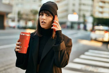 Genç İspanyol kadın akıllı telefondan konuşuyor ve şehirde kahve içiyor..