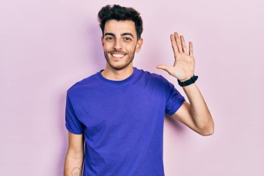 Gündelik tişört giyen genç İspanyol adam beş numarayı gösterip işaret ederken kendinden emin ve mutlu bir şekilde gülümsüyor.. 