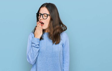 Gündelik kıyafetler ve gözlük takan genç ve güzel bir kadın ağzıyla ağzını kapatmaktan sıkılmış. Huzursuz ve uykulu.. 