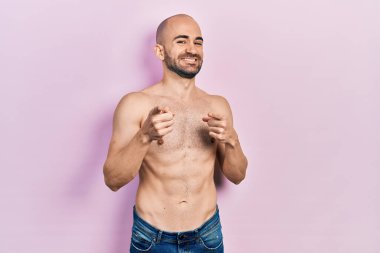 Genç kel adam, mutlu ve komik yüzüyle kameraya parmakla işaret ediyor. iyi enerji ve titreşimler. 