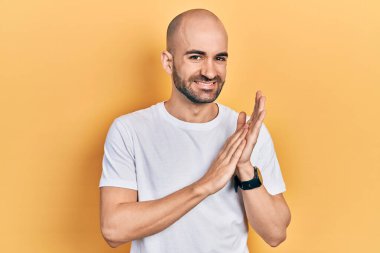 Genç kel adam, günlük beyaz tişörtler giyiyor, alkışlıyor, alkışlıyor, mutlu, mutlu, gururlu eller bir arada. 