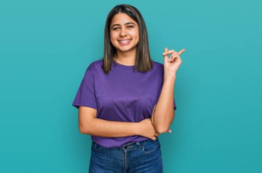 Yüzünde kocaman bir gülümseme olan sıradan mor tişört giyen genç İspanyol kız, kameraya el ve parmak ile bakıyor.. 