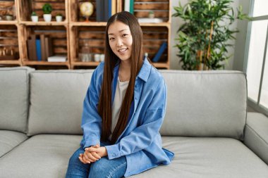 Genç Çinli kız gülümsüyor. Evdeki kanepede mutlu mesut oturuyor..