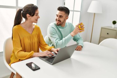 Laptop ve akıllı telefon kullanan genç İspanyol çift evde kahve içiyor..