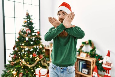 Kızıl saçlı, uzun sakallı, noel şapkası takan, Noel ağacı reddeden, kollarını kavuşturan ve avuç içlerini negatif gösteren, kızgın yüzlü bir adam. 