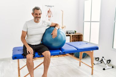 Orta yaşlı İspanyol adam ağrı kesici kliniğinde elinde pilates topuyla kameraya bakıyor. Seksi bir ifadeyle, neşeli ve mutlu bir yüzle.. 