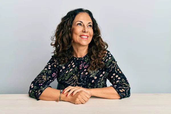 Masaya oturmuş sıradan kıyafetler giyen güzel orta yaşlı bir kadın yüzünde gülümsemeyle yan yana bakıyor, doğal bir ifade. Kendinden emin gülen. 