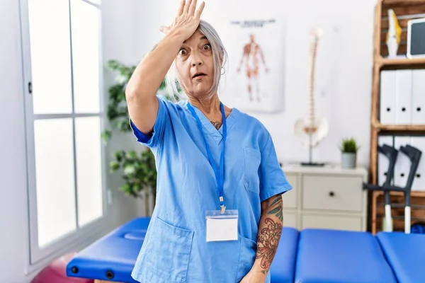 Medelålders Gråhårig Kvinna Bär Sjukgymnast Uniform Läkarmottagningen Förvånad Med Hand — Stockfoto