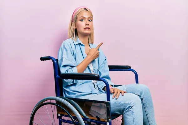 Красивая Блондинка Сидящая Инвалидной Коляске Указывая Сторону Взволнованная Нервная Указательным — стоковое фото