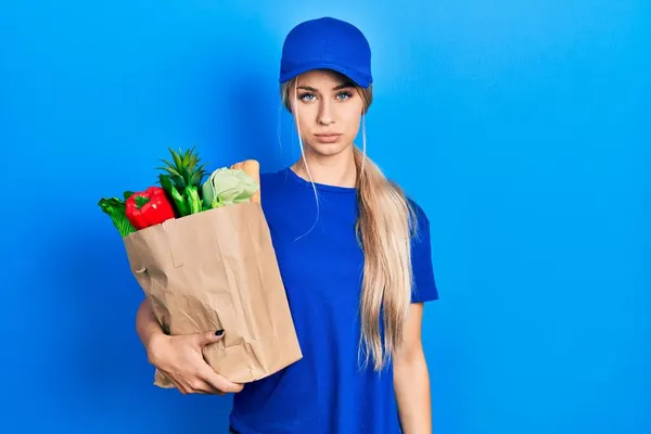 年轻的高加索女人穿着信使制服 带着超市里怀疑和紧张的食品杂货 因为问题皱着眉头 消极的人 — 图库照片