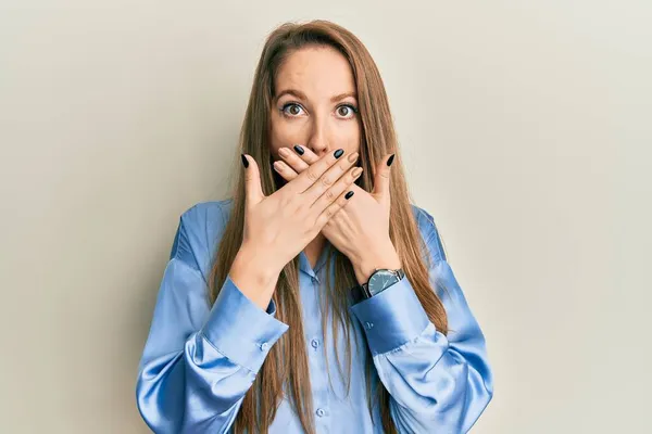カジュアルなブルーのシャツを着た若いブロンドの女性がミスのために手で口を覆いショックを受けた 秘密の概念 — ストック写真