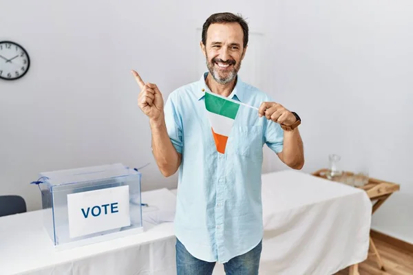 アイルランドの旗を持っている政治選挙でひげを生やしている中年の男笑顔幸せなポインティングで手と指で側面 — ストック写真