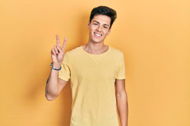 Sarı bir tişört giyen genç İspanyol adam kameraya bakıp zafer işareti yaparken gülümsüyor. İki numara.. 