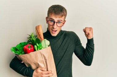 Elinde alışveriş poşeti olan beyaz bir adam gururla bağırıyor zaferi ve başarıyı kutluyor. Kollarını kaldırarak heyecanla bekliyor. 