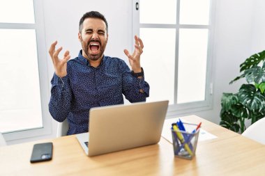 Ofiste çalışan sakallı genç İspanyol adam. Dizüstü bilgisayarla başarıyı kutluyor. Kolları havada ve gözleri kapalı heyecanlı bir şekilde bağırıyor. Kazanan konsept 