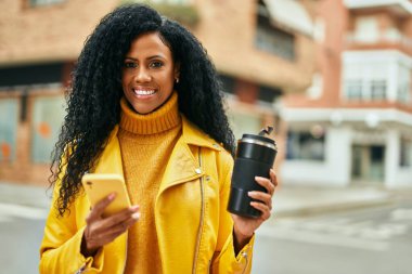 Orta yaşlı Afro-Amerikan kadın akıllı telefon kullanıyor ve şehirde kahve içiyor..