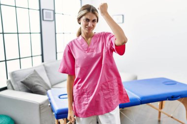 Evde fizyoterapist olarak çalışan genç sarışın kadın öfkeyle bağırırken kızgın ve kızgın bir şekilde yumruk kaldırıyor. öfke ve agresif konsept. 