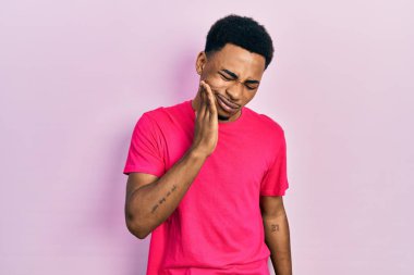 Genç Afro-Amerikan erkek Casua tişörtü giyip diş ağrısı ya da diş hastalığından dolayı ağıza acı dolu bir ifadeyle dokunuyor. dişçi 