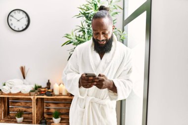 Genç Afro-Amerikan adam, güzellik merkezinde akıllı telefon kullanarak gülümsüyor.