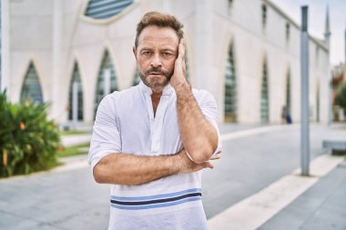 Şehirdeki orta yaşlı bir adam kollarını kavuşturarak depresyondan yorgun ve sıkılmış göründüğünü düşünüyor.. 