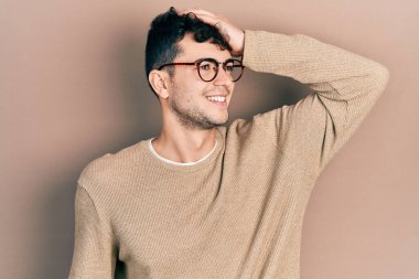 Günlük kıyafetler ve gözlük takan genç İspanyol adam gülümsüyor. Kendine güveniyor, saçlara dokunuyor, el hareketi yapıyor, çekici ve modaya uygun poz veriyor. 