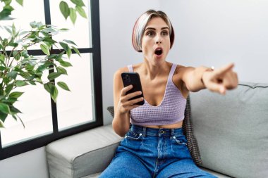 Genç ve güzel bir kadın akıllı telefon ile mesaj yazıyor. Koltukta oturuyor. Parmakla işaret ediyor. 