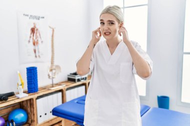 Ağrı kesici kliniğinde çalışan beyaz bir kadın yüksek sesli müzik sesi için kulaklarını parmaklarıyla kapatıyor. sağır kavramı. 