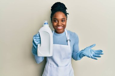 Saçları örülmüş, elinde deterjan şişesi olan Afro-Amerikalı kadın başarıyı mutlu bir gülümsemeyle kutluyor ve kazanan yüz ifadesini kaldırıyor. 