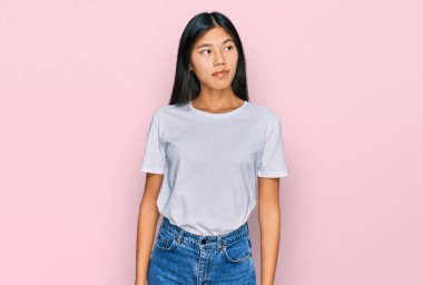 Güzel, genç Asyalı bir kadın, günlük beyaz tişört giyip gülümsüyor, yan tarafa bakıyor ve düşünüyor.. 