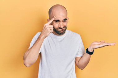 Gündelik beyaz tişört giyen genç ve kel bir adam avuç içi açık fotokopi alanı ve alnını göstermekten rahatsız oluyor. Bunu bir düşün.. 