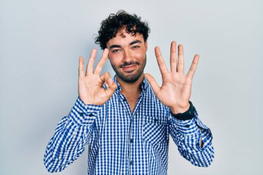 Gündelik kıyafetler giyen genç İspanyol adam sekiz numarayı gösterip işaret ederken kendinden emin ve mutlu bir şekilde gülümsüyor.. 