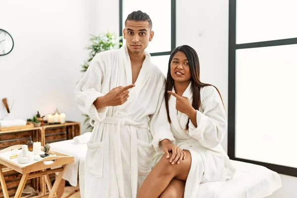 Young Latin Couple Wearing Towel Standing Beauty Center Pointing Aside — Stockfoto