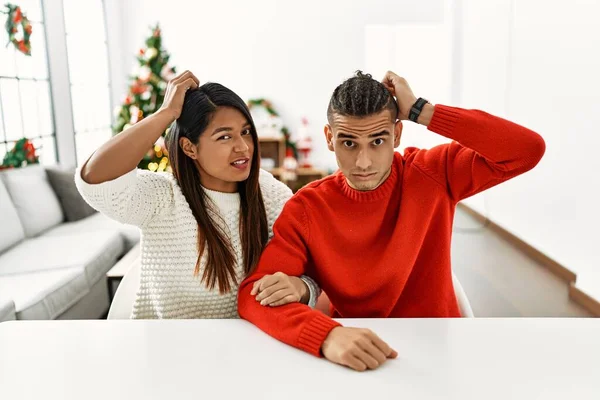 Young Latin Couple Sitting Table Christmas Tree Confuse Wondering Question — Stockfoto
