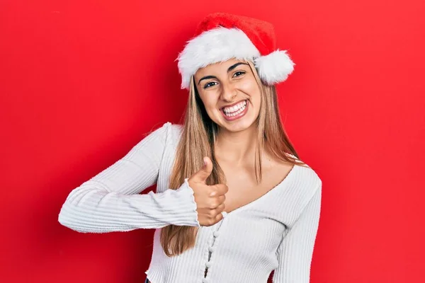 美丽的他惊慌失措的女人戴着圣诞礼帽 手举着幸福的大拇指做手势 赞成的表情看着相机显示的成功 — 图库照片